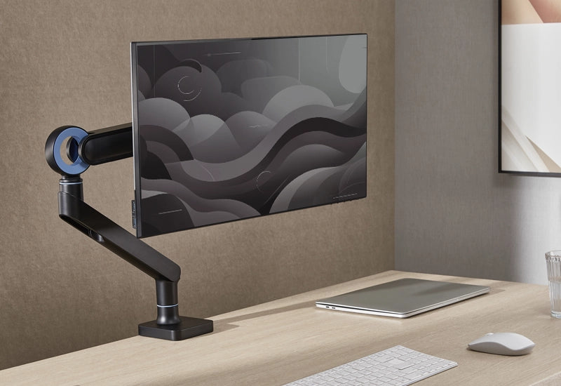 Black monitor arm holding a sleek display screen on a wooden desk.